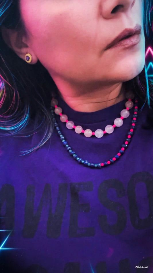 A close-up lifestyle shot of a person wearing a layered necklace. The features two beaded strands: one with translucent light pink round beads and hot pink connectors, and another with dark blue round beads and hot pink connectors.